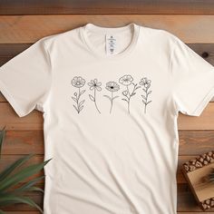 This classic unisex jersey short sleeve Wildflower Tshirt feels soft and light with just the right amount of stretch. It's comfortable and flattering for all. We can't compliment this Botanical shirt enough - it's one of our crowd favorites, and it's sure to be your next favorite too!  100% Airlume combed and ringspun cotton (Heather colors are 52% combed and ring-spun cotton, 48% polyester) Light fabric (4.2 oz/yd² (142 g/m Pre-shrunk fabric Tear-away label Runs true to size -When Can I Expect My Order - Processing Time: 1-3 days During holidays please expect delays as the number of orders are slightly higher than usual, although we will do our best to get your order to you as soon as possible. - Shipping Time - Shipping times average between 2-5 days.  - Care Instructions - Wash items in Botanical Screen Print Short Sleeve T-shirt, Spring Custom Print Tops, Relaxed Fit Short Sleeve Shirt With Plant Print, Botanical Short Sleeve Graphic Shirt, Botanical Graphic Print Short Sleeve Shirt, Botanical Short Sleeve Cotton Tops, White Botanical Screen Print Tops, Botanical Style Short Sleeve Cotton Tops, Botanical Cotton Tops With Short Sleeves