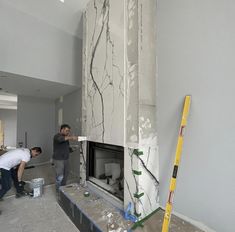 two men working on a fireplace in the middle of a room with paint and plaster