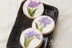 three decorated cookies with flowers on them sitting on a black platter next to a white tablecloth