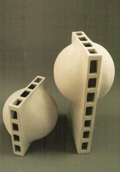 two white vases sitting next to each other on a gray surface, one with holes in it