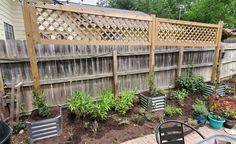 a backyard garden with lots of plants and potted plants on the side of the fence