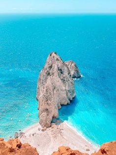 an island in the middle of the ocean with blue water and rocks on it's sides