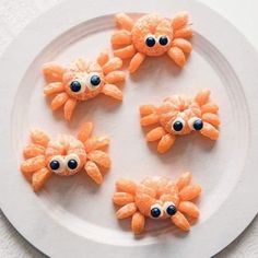 four orange crab cookies on a white plate with blue eyes and one is made out of carrots