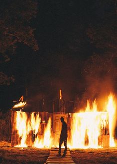 a man standing in front of a fire with flames coming out of the building behind him