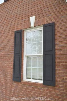 a red brick building with black shutters on the windows and white trim around the window