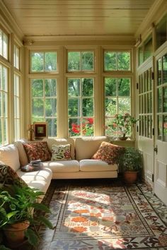 a sun room with couches, potted plants and large windows on the wall