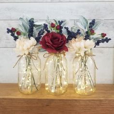 three mason jars with lights and flowers in them