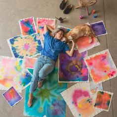 a woman laying on the ground with her dog in front of some colorful art pieces