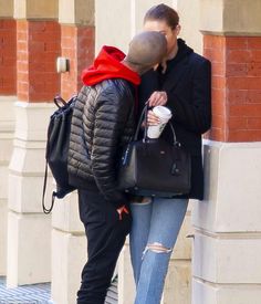 two people standing next to each other near a building and one is kissing the other