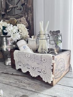 an old wooden box with white flowers and other items in it sitting on a table