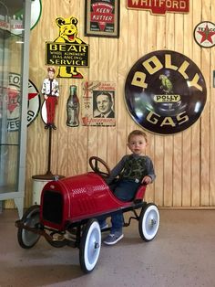 a young boy sitting in a red pedal car with white wheels and spoked tires