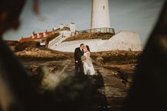 a bride and groom standing in front of a lighthouse