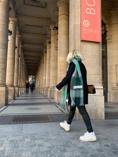 a woman is walking down the sidewalk in front of an old building with columns and pillars