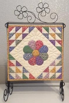 a quilted table top with metal stand holding a colorful flower design on it's side