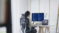 a woman sitting in front of a computer desk with a monitor and keyboard on it