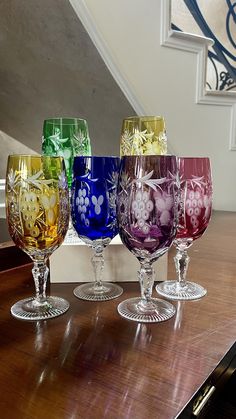 four wine glasses sitting on top of a wooden table next to a stair case in a home