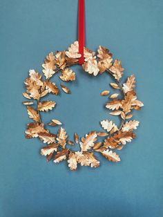 a christmas wreath hanging from a red ribbon on a blue background with gold leaves and acorns