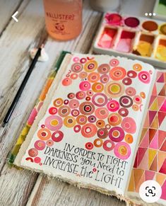 an open book sitting on top of a wooden table next to paintbrushes and paints