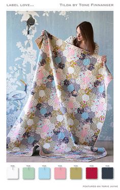 a woman holding up a quilt in front of a wall