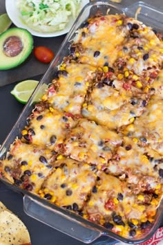 an enchilada casserole in a glass dish with tortilla chips and avocado on the side