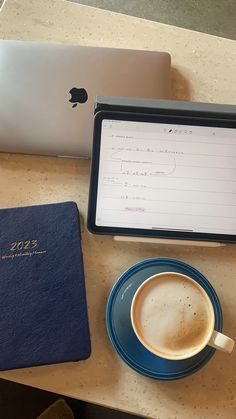 an apple laptop computer sitting on top of a table next to a cup of coffee