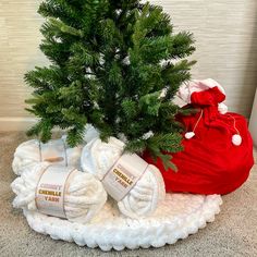 a small christmas tree in a red bag next to some white yarn and a crocheted santa sack