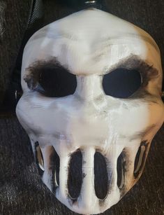 a white skull mask with black eyes on a carpeted floor next to a cell phone