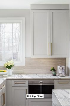 a kitchen with white cabinets and marble counter tops, along with a vase filled with flowers