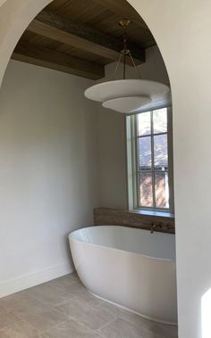 a large white bathtub sitting under a window next to a wall mounted light fixture