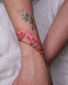 a woman's arm with pink flowers on it and green leaves in the middle