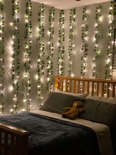 a teddy bear laying on a bed in front of a wall covered with string lights