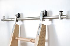 a pair of wooden pegs hanging from a metal bar on the wall next to a white wall