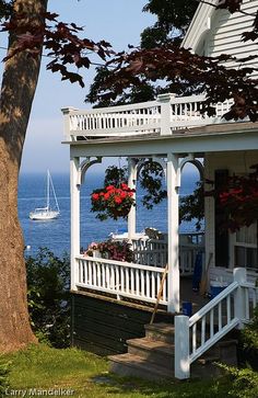 a white house sitting on top of a lush green hillside next to the ocean with boats in the water