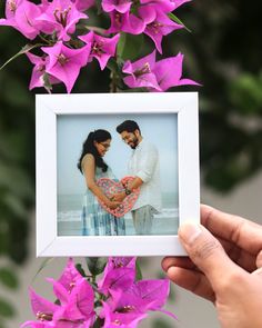 a person holding up a heart shaped photo with purple flowers in the foreground and behind them