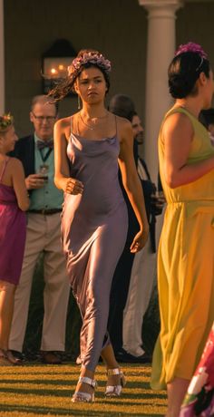 a woman in a purple dress is walking with other people behind her on the grass