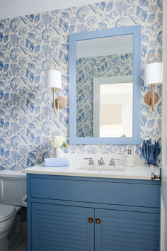 a bathroom with blue and white wallpaper has a large mirror above the sink, along with two lamps on either side of the vanity