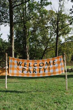 an orange and white welcome party banner in the grass with trees behind it on a sunny day