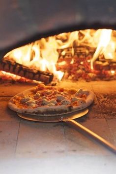 two pizzas sitting in front of an oven with flames coming from the top and bottom