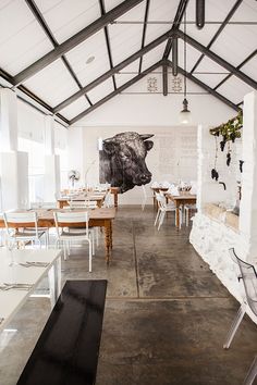 an empty restaurant with tables and chairs in the center, near a cow painting on the wall