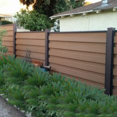 an outside view of a house with a fence in the foreground and plants on the other side