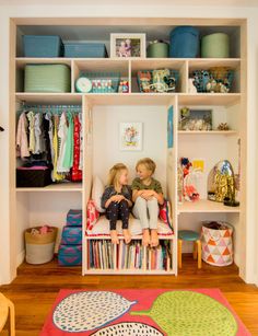 two children sitting on a bench in front of a closet full of toys and books