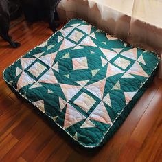 a dog standing next to a green and white quilted bed on top of a wooden floor