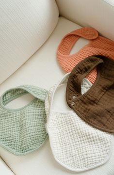 three bibs sitting on top of a white couch next to each other in different colors