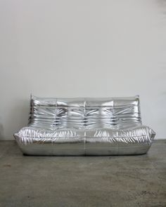 a shiny metal couch sitting on top of a cement floor next to a white wall