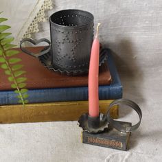 a pink candle sitting on top of a stack of books next to a metal cup