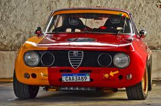 an orange and red car parked in front of a stone wall with the number plate causa388