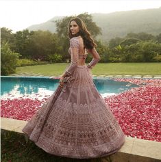 a woman standing in front of a pool wearing a pink gown with long sleeves and open back