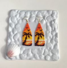 a pair of beaded earrings sitting on top of a white plate next to a seashell