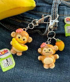 two monkey keychains sitting on top of a pair of jeans next to a banana