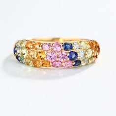 a gold ring with multicolored stones on the inside and outside, sitting on a white surface